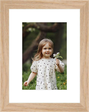 "Framed photo of a young girl holding a flower in an outdoor setting. "