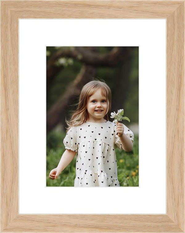 "Framed photo of a young girl holding a flower in an outdoor setting. "