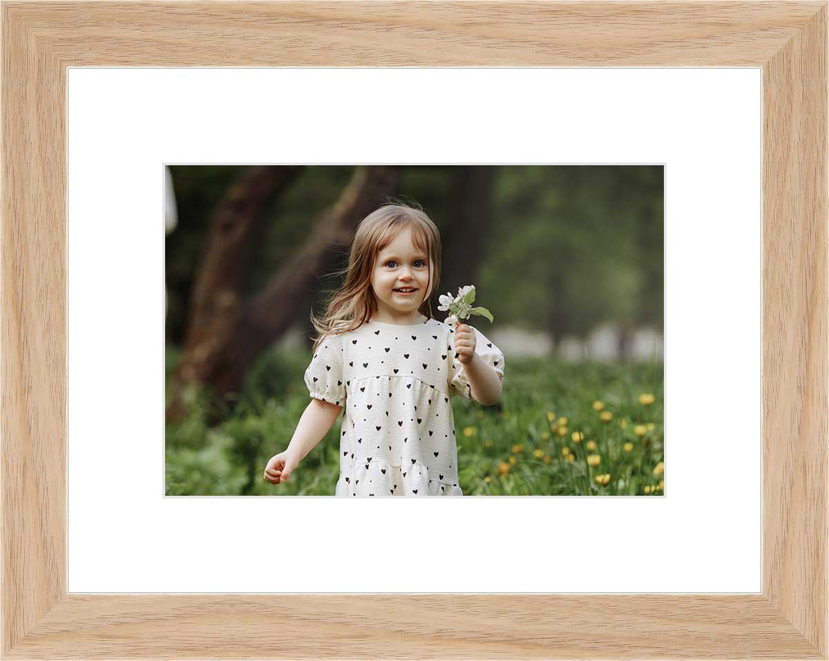 Framed photo of a young girl holding flowers, set in a light wood frame with white matting.