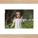 Framed photo of a young girl holding flowers, set in a light wood frame with white matting.