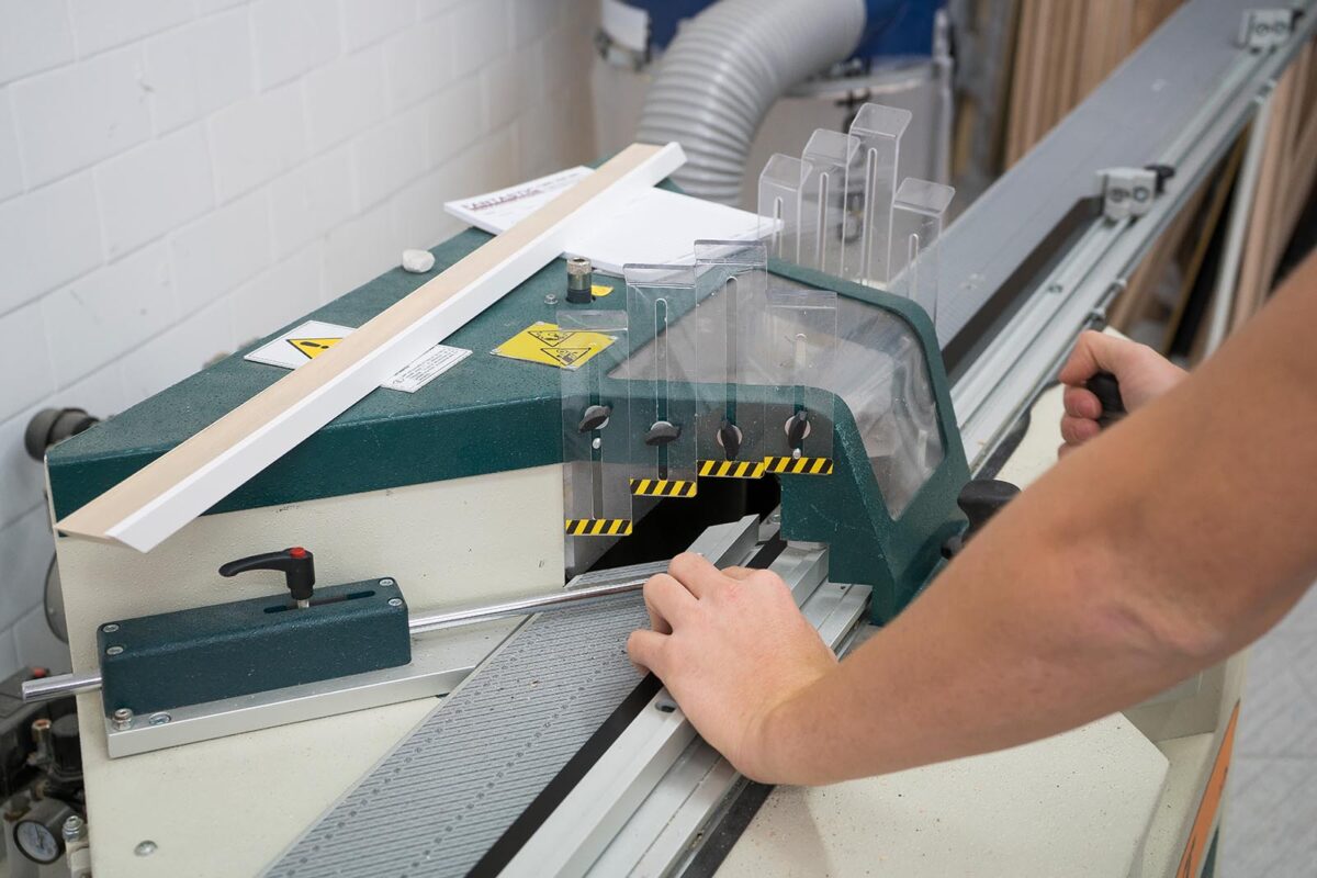 Close-up of a framing machine cutting a piece of molding, with hands guiding the material through the process.